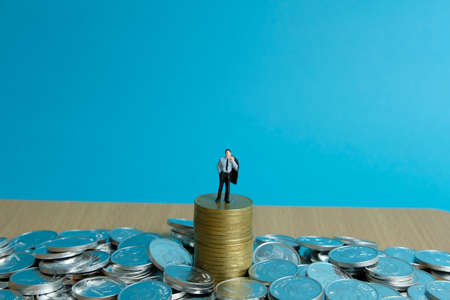 Miniature business concept - a depressed businessman standing on gold coin stackの写真素材