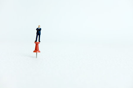 Miniature business concept - a businessman standing on a thumbtack / push pin with white backgroundの写真素材