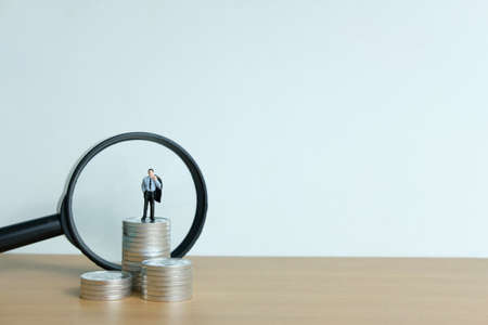 Miniature people concept - a businessman standing on coin stack with magnifier glassの写真素材