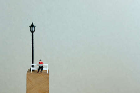 Young man sitting on white chair under a outdoor lamp while reading a bookの写真素材