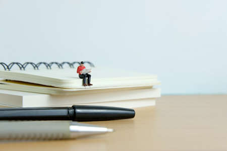 Young man sitting on book pile while reading with pen in front of itの写真素材