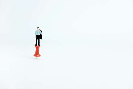 Miniature business concept - a businessman standing on a thumbtack / push pin with white backgroundの写真素材