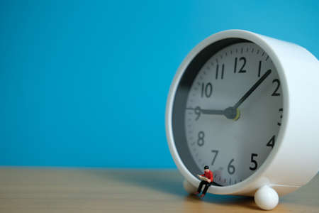 Miniature people for morning reading time concept - young man seating above clock reading a bookの写真素材