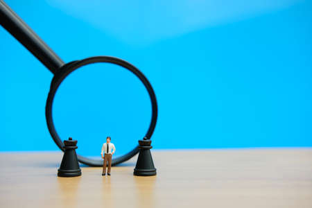 Miniature people strategic concept - businessman standing between castle chess pawn in front of magnifier glassの写真素材