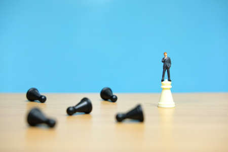 Business strategy conceptual photo - miniature businessman standing on castle chess piece in between falling chess pieceの写真素材