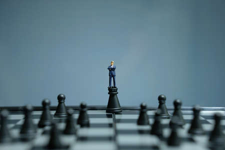 Business strategy conceptual photo - miniature businessman standing above castle pawn in the middle of chessboardの写真素材