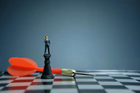 Business strategy conceptual photo - miniature businessman standing above castle pawn on a chessboard with red arrowの写真素材