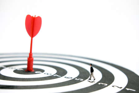 Business strategy conceptual photo - Miniature businessman walking toward red arrow at the center of...