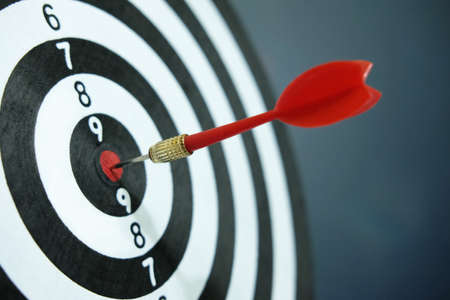 Conceptual photo of business strategy / accuracy - a red arrow that sticks directly in the center of the target dartboardの写真素材
