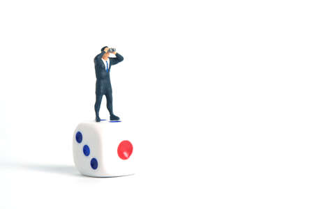 Miniature people toys photography. A businessman looking, searching, observing using binoculars above the dice isolated on white background.の写真素材