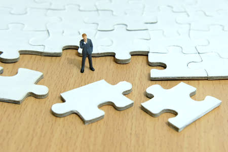 Business strategy conceptual photo - Miniature businessman thinking in front of scattered puzzlesの写真素材