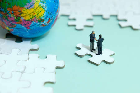 Business strategy conceptual photo - Miniature businessman make handshake partnership above jigsaw...