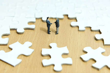 Business strategy conceptual photo - Miniature businessman make handshake partnership in the center of jigsaw puzzle pieceの写真素材