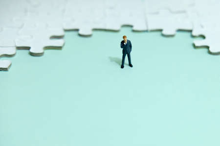Business strategy conceptual photo - Miniature businessman thinking in front of puzzle jigsawの写真素材