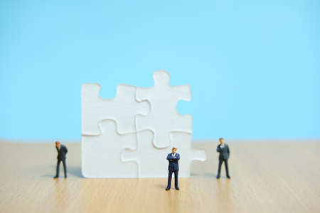 Business strategy conceptual photo - Group of miniature businessman standing on wooden table in front of missing piece puzzleの写真素材
