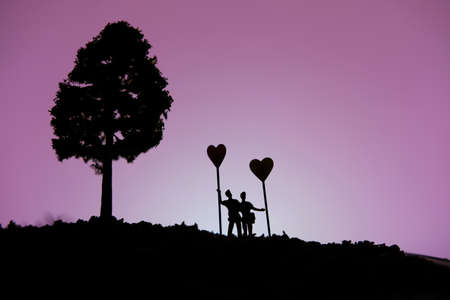 miniature people / toy photography - conceptual valentine holiday illustration. A Couple silhouette standing at the hill holding heart balloonの写真素材