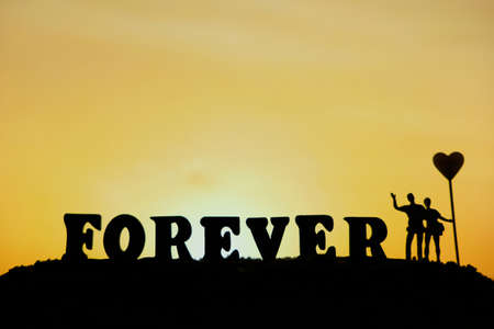 miniature people / toy photography - conceptual valentine holiday illustration. Happy couple holding each other holing heart balloon with forever word blockの写真素材