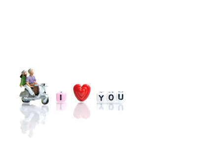Miniature people photography for valentines day, young couple riding scooter with I love you beads on shiny white background. Image photoの写真素材