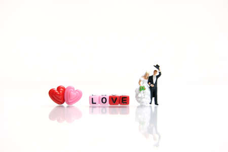 Miniature people photography for valentines day, bride and groom with heart shape and love word beads on shiny white background. Image photoの写真素材
