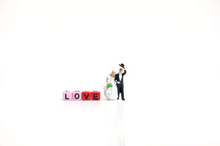 Miniature people photography. Bride and groom with love word beads on shiny white backgroundの写真素材