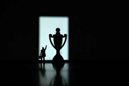 Business strategy conceptual photo - Silhouette of miniature businessman pointing on winning trophy...