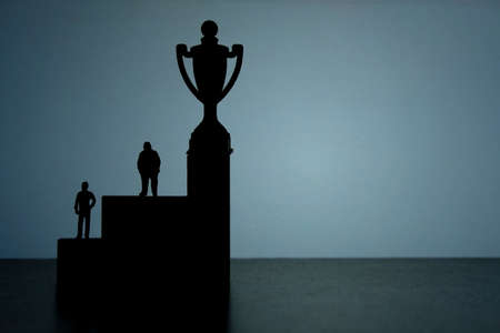 Business strategy conceptual photo - Silhouette of miniature businessman standing on podium to reach winning trophyの写真素材