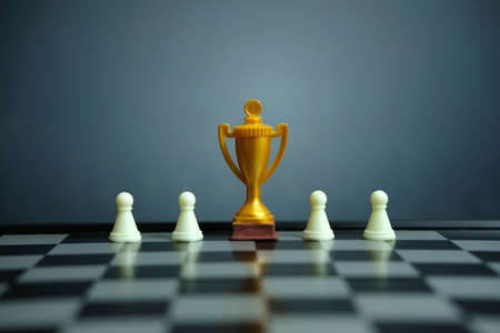 Business strategy conceptual photo â Golden trophy standing on chessboard with chess pawnの写真素材