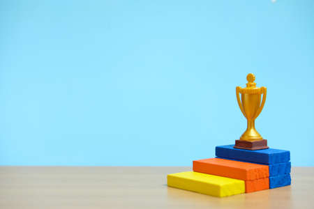 Golden trophy standing at colorful podium on wooden tableの写真素材