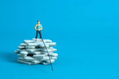 Miniature toy photography people. Fisher standing above white puzzle jigsaw stack. Isolated on blue background.の写真素材