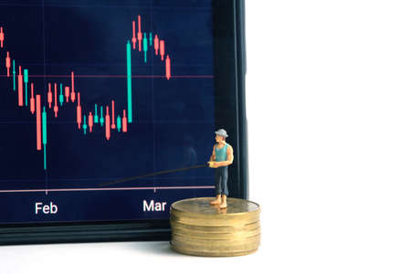 Miniature people toy photography. An angler standing above coin money stack searching investment profit, opened candle chart from stock market app. Isolated on white background.の写真素材
