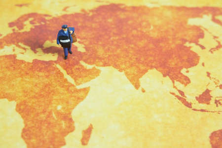 Miniature people toys conceptual photography. Global, international delivery service. Postman, courier standing above map.の写真素材