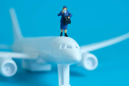 Miniature people toys conceptual photography. Airplane parcel package delivery. Postman courier with white plane, isolated on blue background.の写真素材