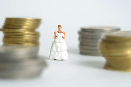 Wedding dress budget for bride, miniature people illustration concept. Woman standing between coin money stack. Image photoの写真素材