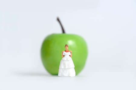 Diet plan before wedding or marriage day concept. Woman standing in front of apple with trying wedding dress. Miniature people, toys photography.の写真素材