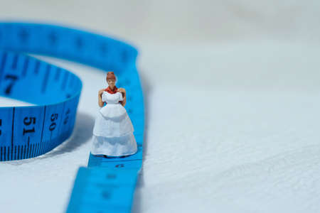 Women miniature people standing above measuring tape to fix her wedding dress. Image photo