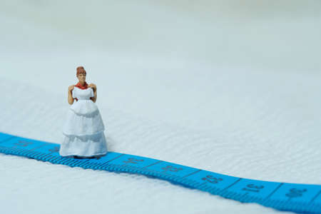 Women miniature people standing above measuring tape to fix her wedding dress. Image photoの写真素材