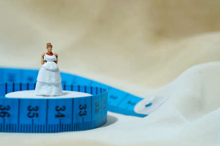 Women miniature people standing above measuring tape to fix her wedding dress. Image photo
