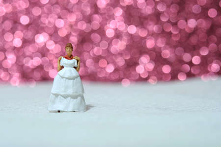 Women miniature people stand above white tile trying wedding dress with bokeh pink light background. Image photoの写真素材