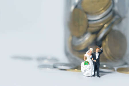 Wedding budget concept miniature people, toys photography. Bride and groom with coin money on a jar glass isolated on white background. Image photoの写真素材
