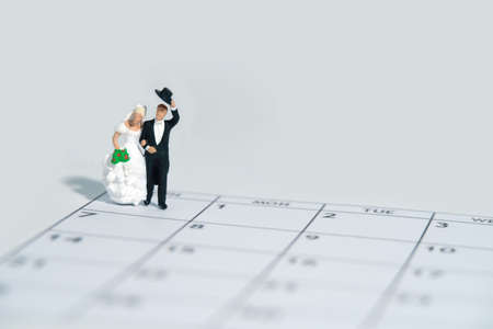 Wedding marriage day, schedule date celebration concept miniature people toy photography. Bride and groom standing above calendar. Image photoの写真素材