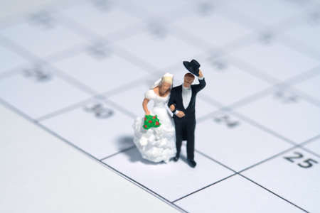 Wedding marriage day, schedule date celebration concept miniature people toy photography. Bride and groom standing above calendar. Image photoの写真素材