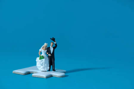 Bride and groom married miniature people stand above white puzzle jigsaw, isolated cut out on a blue background. Wedding plan strategy and choice. Image photoの写真素材