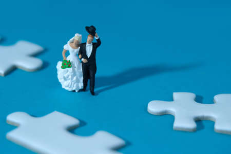 Bride and groom married miniature people standing between three white puzzle jigsaw, isolated cut out on a blue background. Wedding plan strategy and choice. Image photoの写真素材