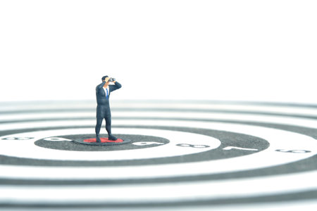 Businessmen standing above dartboard using binoculars. Miniature tiny people toys photography. isolated on white background.の写真素材