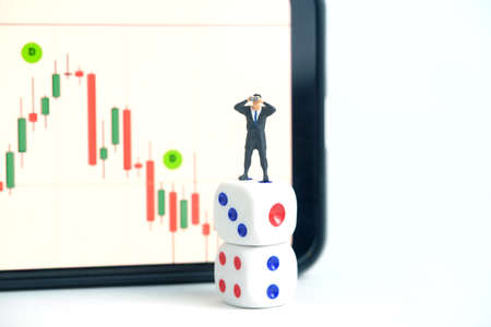 Businessman using binoculars standing above dice, investing in stock market without analyzing the candle stick chart. Miniature tiny people toys photography.の写真素材