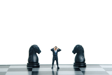 Businessman using binoculars standing in between horse knight chess pawn. Miniature tiny people toys photography. isolated on white background.の写真素材