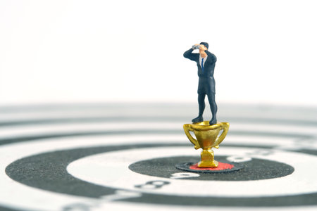 Businessmen standing above golden trophy on dartboard using binoculars. Miniature tiny people toys...