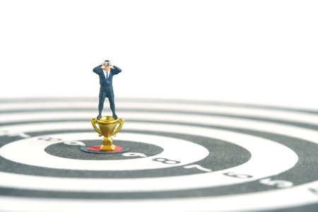 Businessmen standing above golden trophy on dartboard using binoculars. Miniature tiny people toys photography. isolated on white background.の写真素材