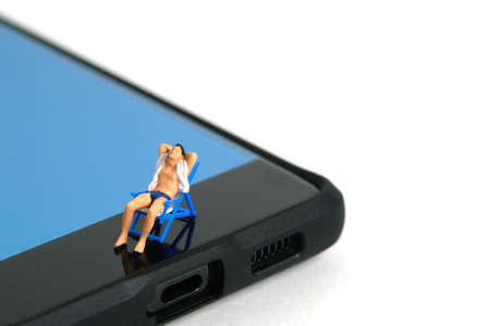 Miniature people toy figure photography. Virtual travel concept, Men relaxing seat at chair above smartphone, isolated on white background. Image photoの写真素材