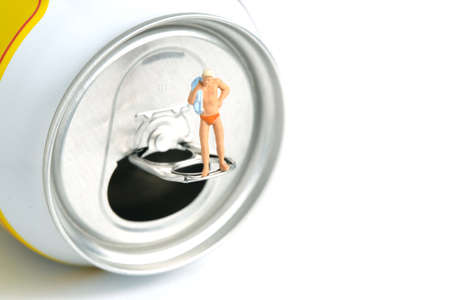 Miniature people toy figure photography. Creative summer vacation concept. A men standing above soft drink canned getting ready to swim. Image photoの写真素材